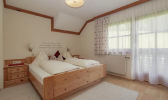 A cozy bedroom with a wooden double bed. Large windows let in a lot of light and offer a view outside.