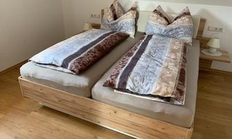 A cozy bedroom with two separate beds and decorative pillows. The floor is made of light wood and the walls are plain and bright.