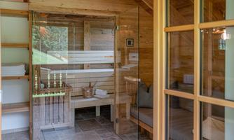 A cozy wellness area with a wooden sauna and a comfortable seating area. Large windows provide plenty of daylight and a view outside.