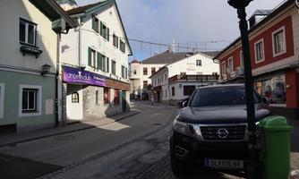 A picturesque street with charming buildings in the Austrian style. A car is parked while the clouds cover the sky.