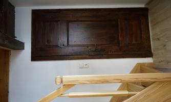 A rustic wooden door in a bright room. In the foreground, there is a staircase made of light wood.