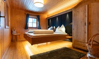 A cozy bedroom with wooden paneling and a floating bed. The room has large windows with blue curtains and a warm, inviting carpet.
