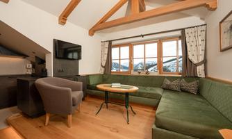 A cozy living room corner with a green sofa and a round table. Large windows offer a view of the mountains.