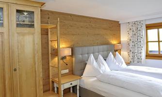 A cozy bedroom with a comfortable double bed and modern wooden paneling. On the wall, there is a dresser and a window with a floral curtain.