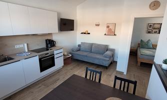 A modern and bright apartment with an open kitchen and a cozy living room. There is a dining table and a couch, as well as a separate sleeping area in the back.