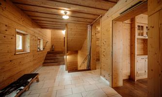 A cozy entrance area with wooden paneling and bright tiles. A staircase leads to the upper floors, while an open kitchen is visible on the right side.