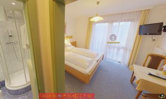 A bright hotel room with a double bed and a table. The room has a bathroom and a television.