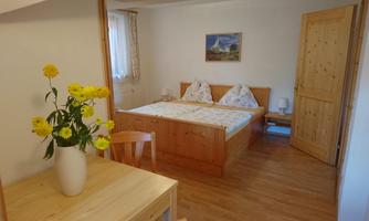 A cozy bedroom with a double bed and wooden details. A vase with yellow flowers is on the table.