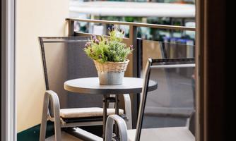 A small balcony with a round table and two chairs. On the table sits a flower pot with a plant.