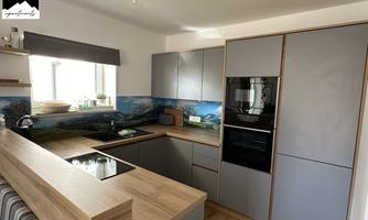 Modern kitchen with wooden countertop and gray cabinets. A window allows for plenty of daylight and a picturesque wall design in blue and green.
