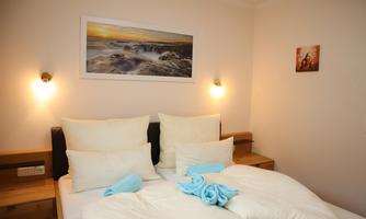 A cozy bedroom with a double bed and comfortable pillows. On the wall, there are a landscape painting and a small piece of art.