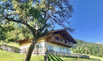 A cozy house with a beautiful balcony and adjacent garden. In the background, lush meadows and trees can be seen.