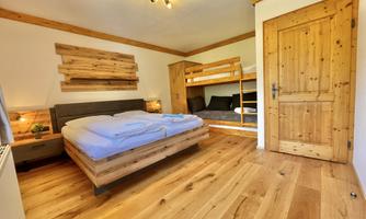 A cozy room with a double bed and a bunk bed. The floor is made of wood, and the walls are in warm tones.
