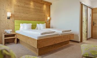 A modern bedroom with a wooden double bed and bright cushions. The walls are made of light wood, and the room is well lit.