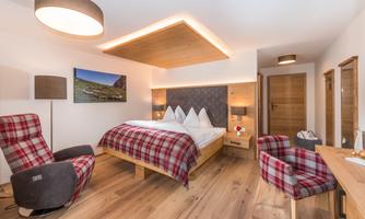 A modern bedroom with wooden interiors and comfortable armchairs. Large windows provide plenty of natural light.