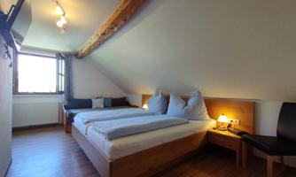 A cozy bedroom with a double bed and two pillows. The room has wooden floors and a window that provides daylight.