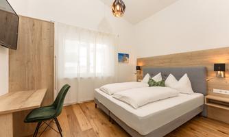 A modern bedroom with a comfortable double bed and a desk. Large windows provide plenty of natural light.