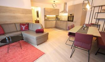 A modern living and dining room with a comfortable couch and a large dining table. The kitchen is open and well-equipped.