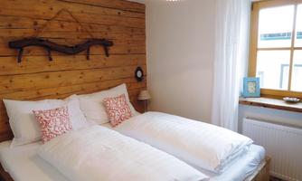A cozy bedroom with two single beds and a wooden wall. A window with plenty of natural light and a simple, stylish decor.