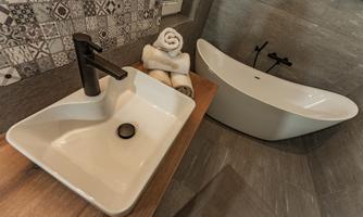 A modern bathroom with an elegant sink and a freestanding bathtub. Clean towels are ready, and a decorative wall paneling adds style.