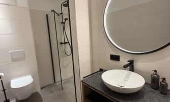 A modern bathroom with an elegant sink and a large mirror. The shower is open and the walls are brightly tiled.