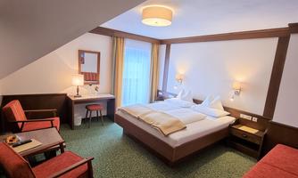 A cozy hotel room with a double bed and modern furnishings. There is a desk, a table with chairs, and large windows that let in plenty of light.