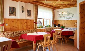 A cozy restaurant with wooden walls and red tablecloths. The decor is rustic and inviting with plants and windows for natural light.