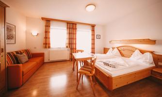 A cozy room with a double bed, a table, and chairs. Bright curtains and warm wood create an inviting atmosphere.