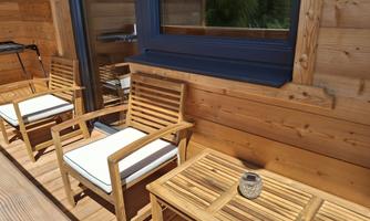 A cozy outdoor area with two wooden chairs and a table. The wooden paneling creates a warm atmosphere.