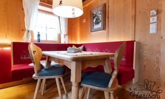 A cozy dining area with a wooden table and two chairs. The walls are made of wood, and the windows let in plenty of light.