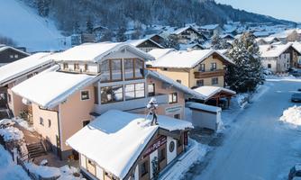 A snow-covered landscape with charming houses and a peaceful village. The sky is clear and the mountains are visible in the background.
