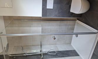A modern bathroom with a glass shower and an elegant toilet. The walls are in neutral tones.