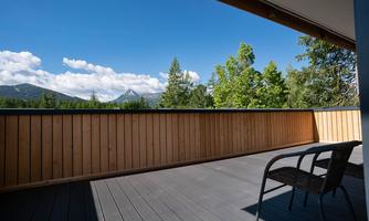 A balcony with a view of green trees and mountains under a blue sky. A chair is ready for relaxation.
