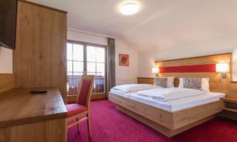 A modern bedroom with two beds, wooden furniture, and a red carpet. A desk and a TV are also available.