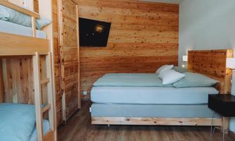 A modern bedroom with wooden walls. There is a double bed, a loft bed, and a television on the wall.