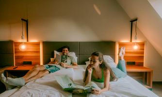 A cozy bedroom with two beds. A couple is relaxing while reading a book and browsing through a magazine.