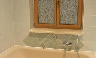 A modern bathroom with a bathtub and a large window. The walls are light tiled and have gray accents.