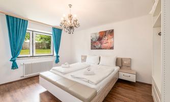 A modern bedroom with a large bed and bright furnishings. The blue curtains and chandelier give the room a cozy atmosphere.