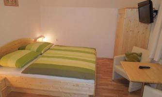 A cozy bedroom with a wooden bed and striped blankets. There is a table, a chair, and a television on the wall.