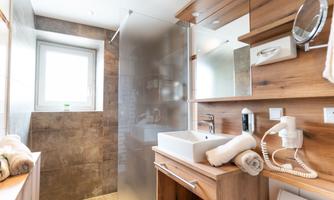 A modern bathroom with wood paneling and light tiles. The shower is separated by a glass wall and towels as well as toiletries are visible.