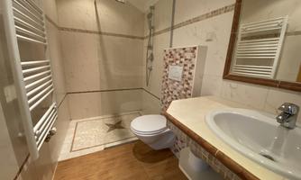 A modern bathroom with shower, sink, and toilet. The walls are light tiled and there is a radiator.