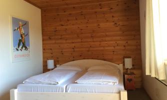 A cozy bedroom with a double bed and wooden paneling. On the wall hangs a poster of an Austrian landscape.