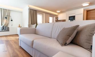 A modern living room with a white sofa and two cushions. Bright colors and large windows create an inviting atmosphere.