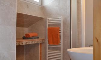 A modern bathroom with a shower cabin and a toilet. A towel in orange and a pleasant, bright atmosphere create an inviting mood.