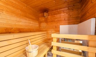 A cozy sauna with wooden paneling and short benches. In the foreground, there is a wooden bucket with a spoon.