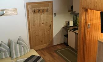 A cozy room with a wooden ceiling and a double bed. There is a small kitchen and access to the door.