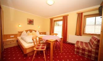 A cozy room with a double bed and a table. Red carpets and curtains give the space an inviting atmosphere.