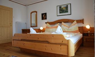 A cozy bedroom with a large wooden bed and colorful pillows. Pictures hang on the walls, and a pleasant atmosphere is created by the warm light.