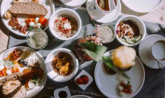 A beautifully set table with various breakfast dishes. There is bread, yogurt, fruit, and drinks.