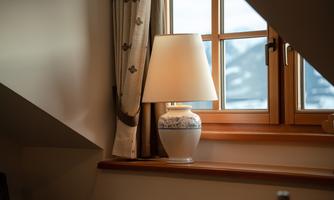 A lamp on a windowsill with a beautiful design is next to a window through which one can see the mountains. The room is cozy and bright.